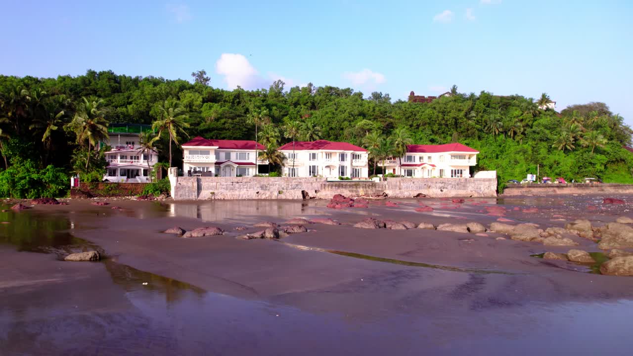 Vista sul mare della spiaggia costiera con ville e colline verdi a Quegdevelim Beach, Goa, India. Orario diurno, carrellata in avanti, ripresa con drone, 4K