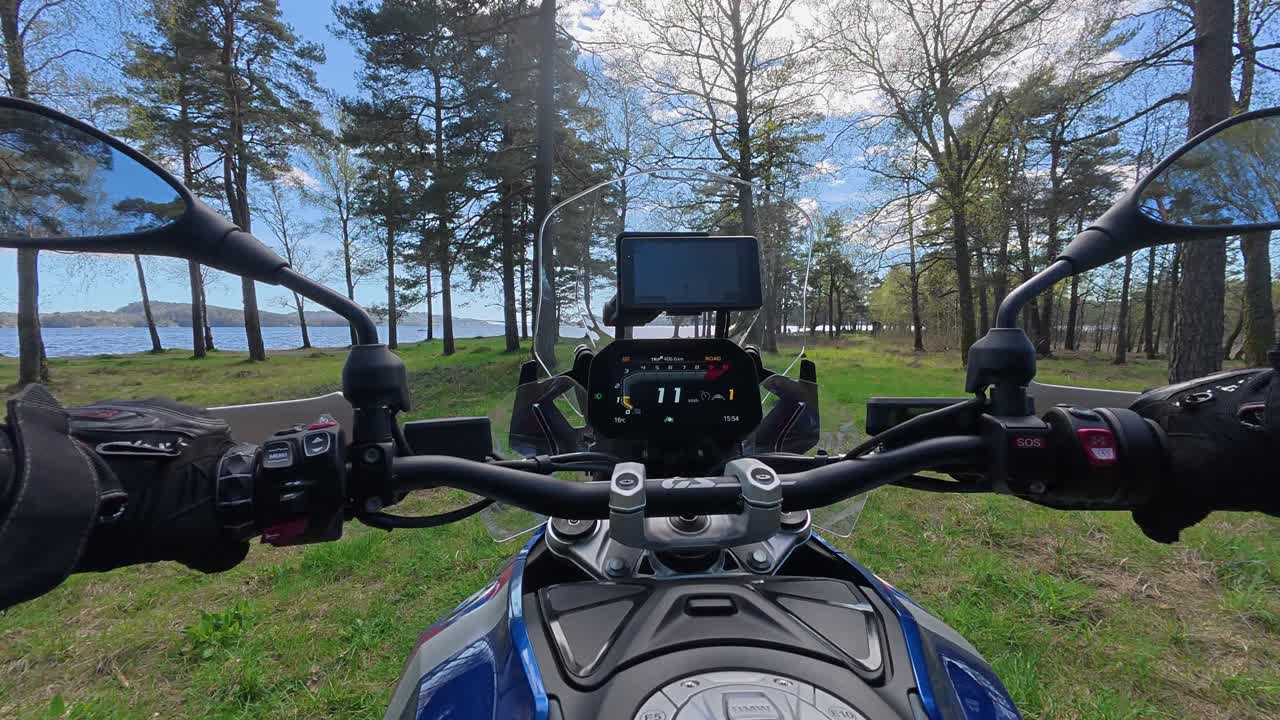 Filmato POV con action camera montata sul petto di una motocicletta da avventura che percorre lentamente una strada sterrata attraverso la foresta verso una spiaggia. Tempo soleggiato estivo con erba verde, alberi e paesaggi costieri. Ideale