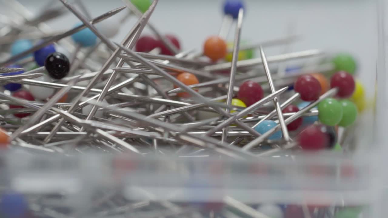 Macro close up of colorful metallic sewing pins with round heads inside transparent plastic container