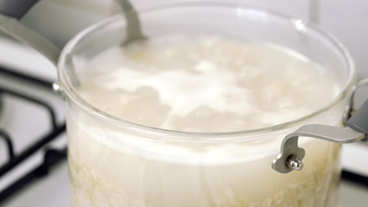 feche a panela de vidro no fogão enquanto cozinha a sopa de arroz, água fervente com bolhas sobre a água