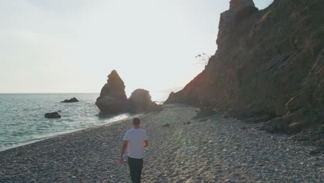 Man-walking-at-the-beach,-drone-flying-by-forward