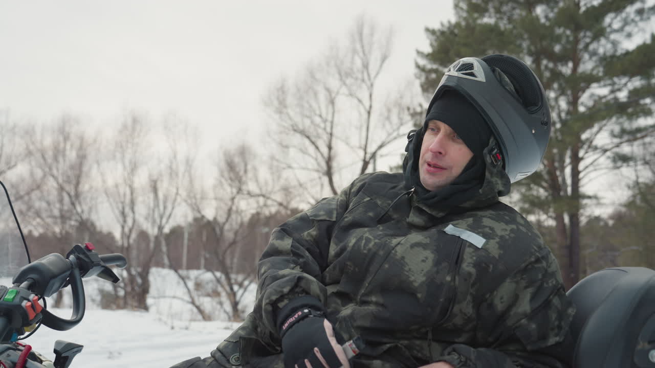 Pilota che si riposa sulla motoslitta, esalando vapore in una radura innevata nel bosco; un uomo con casco e giacca mimetica si reclina sul sedile, respiro e vapore visibili, pini e neve polverosa tutt'intorno, luce invernale calma.