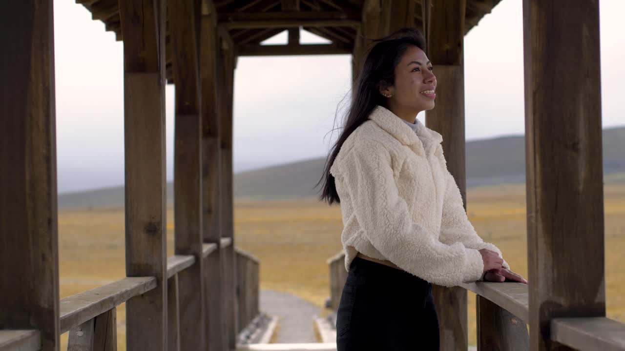 Woman fixes hair and walks to other side of bridge smiling enjoying view