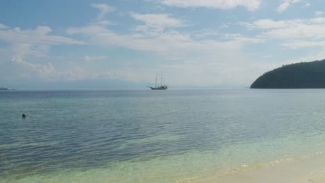 Traditional-sailing-boat-floats-in-a-distance-on-the-turquoise-waters-of-Raja-Ampat,-Indonesia