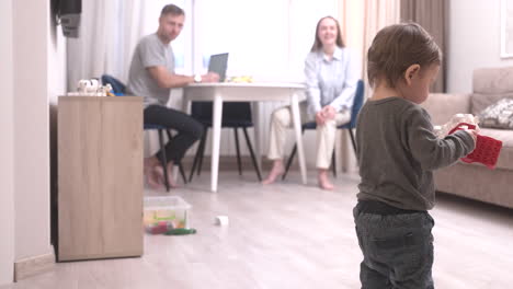 baby playing with toys at home, then twalking towards the table where his parents are sitting