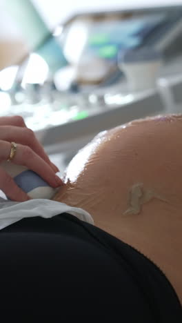 pregnant woman having ultrasound check up. doctor's hand moves the sensor by the belly covered with gel. vertical video