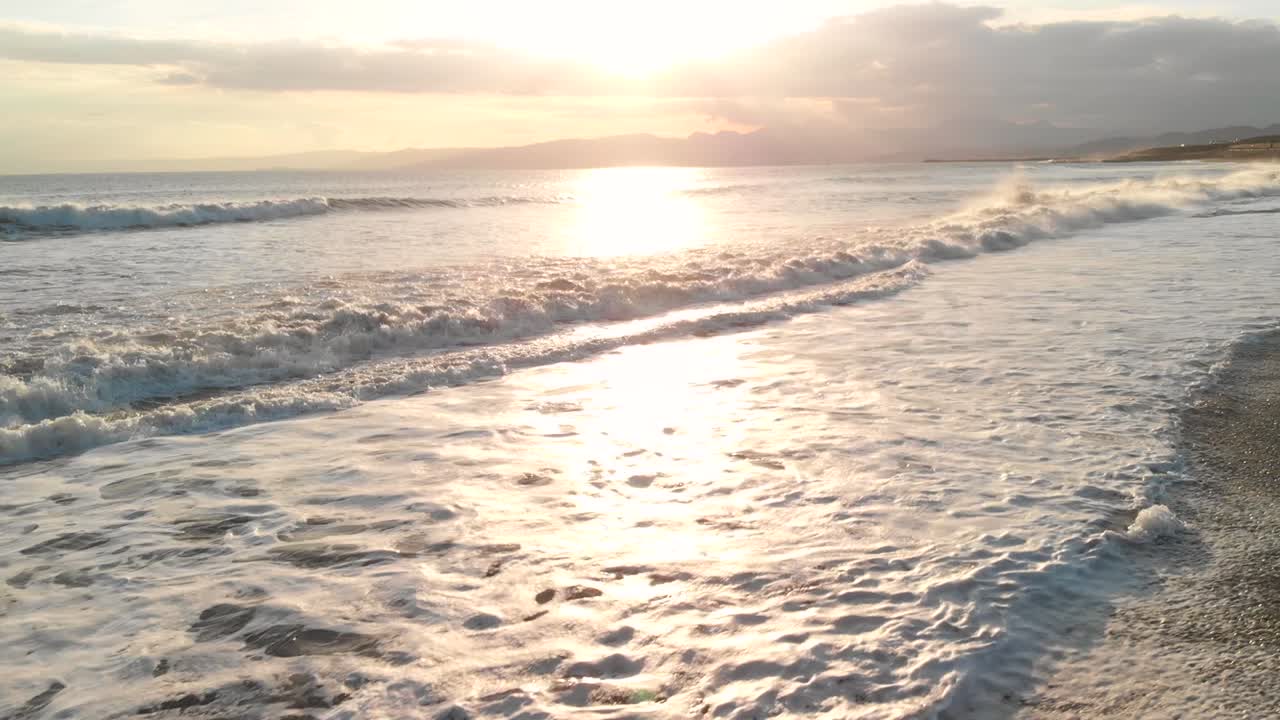 수위 슬로우 모션에 가까워지면서 일몰 해변에서 충돌하는 파도 위로 공중 상향 비행