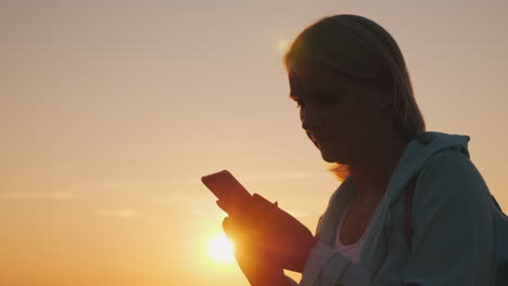 silhouette of a middle-aged woman using a smartphone at sunset