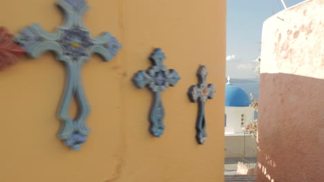 souvenir style colorful crosses hang on an orange wall in an alley close to the famous blue dome chapel in oia santorini