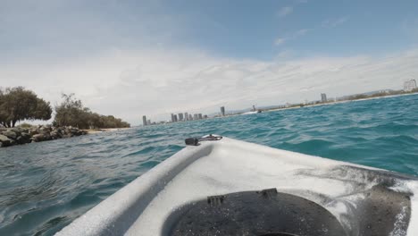 fpv of a kayak drifting in the ocean near jet skis towards a city skyline
