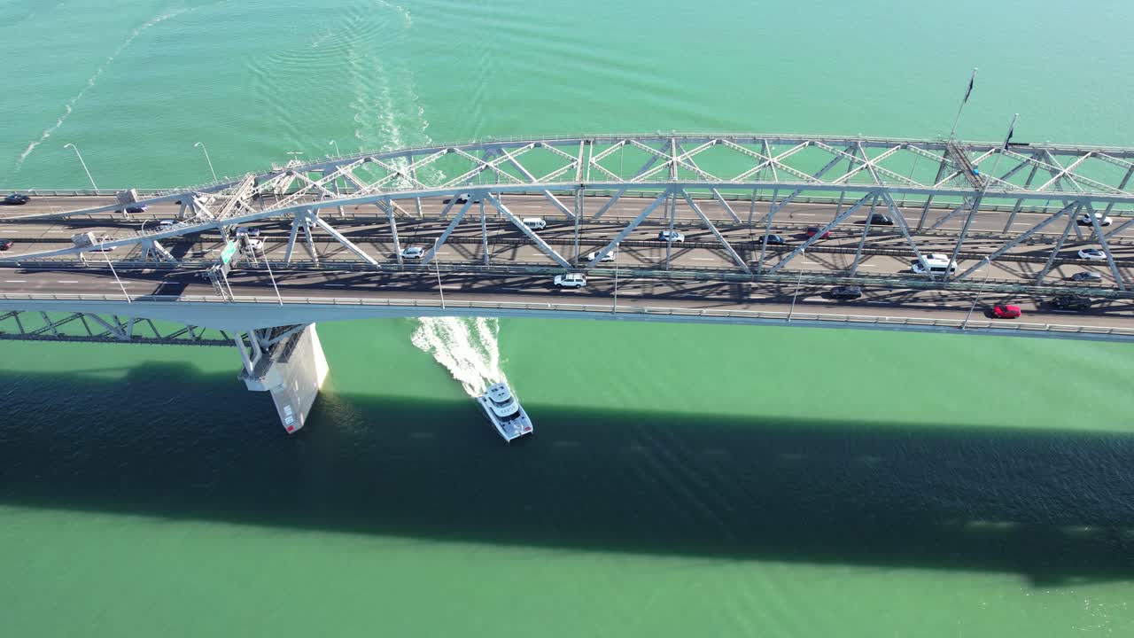 뉴질랜드의 오클랜드 하버 브릿지 아래에서 카타마란 보트와 함께 박스 트러스 구조물을 통과하는 차량