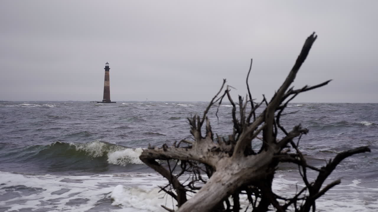 el faro de la isla morris frente a la costa de carolina del sur en segundo plano mientras las olas chocan en primer plano