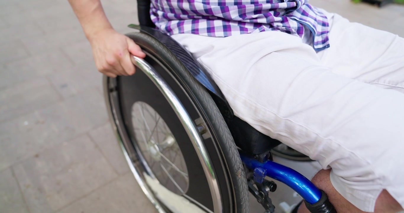 Primo piano della mano di una persona che spinge la ruota di una sedia a rotelle all'aperto