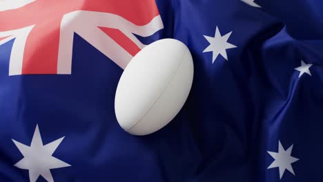 White-rugby-ball-over-waving-flag-of-australia-with-copy-space,-in-slow-motion