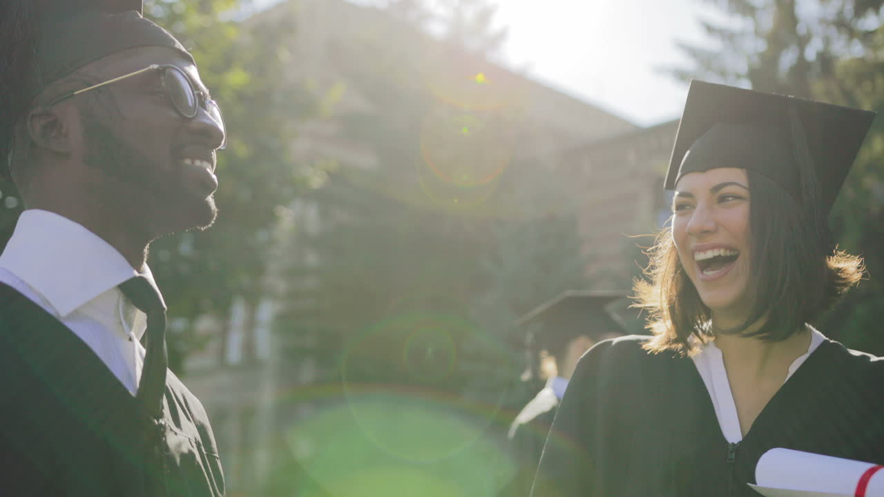 Close up young multi ethnical graduates in caps laughing out loud and having fun on their graduation day