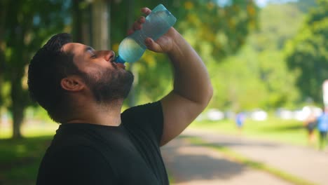 Portrait-of-male-taking-a-sip-of-water-from-bottle-after-exercise-in-the-park-in-slow-motion