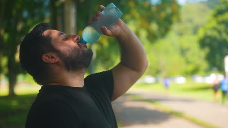 portrait of male taking a sip of water from bottle after exercise in the park in slow motion