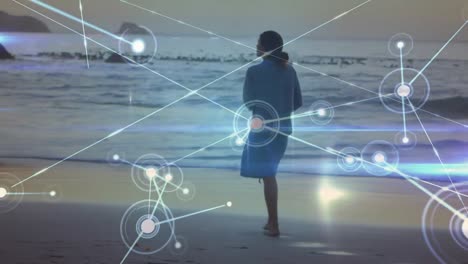 animation of networks of connections over caucasian woman walking on beach