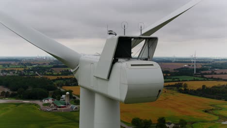 wind turbine from behind with an aerial drone close up orbital shot panning around with farmland in the background