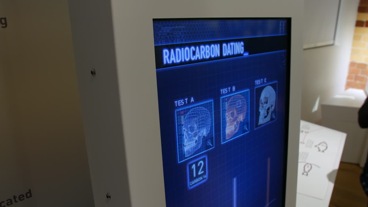 A crime lab scientist using a touchscreen display showing a radiocarbon dating analysis of three skulls for scientific research, archaeology, and the study of ancient remains.