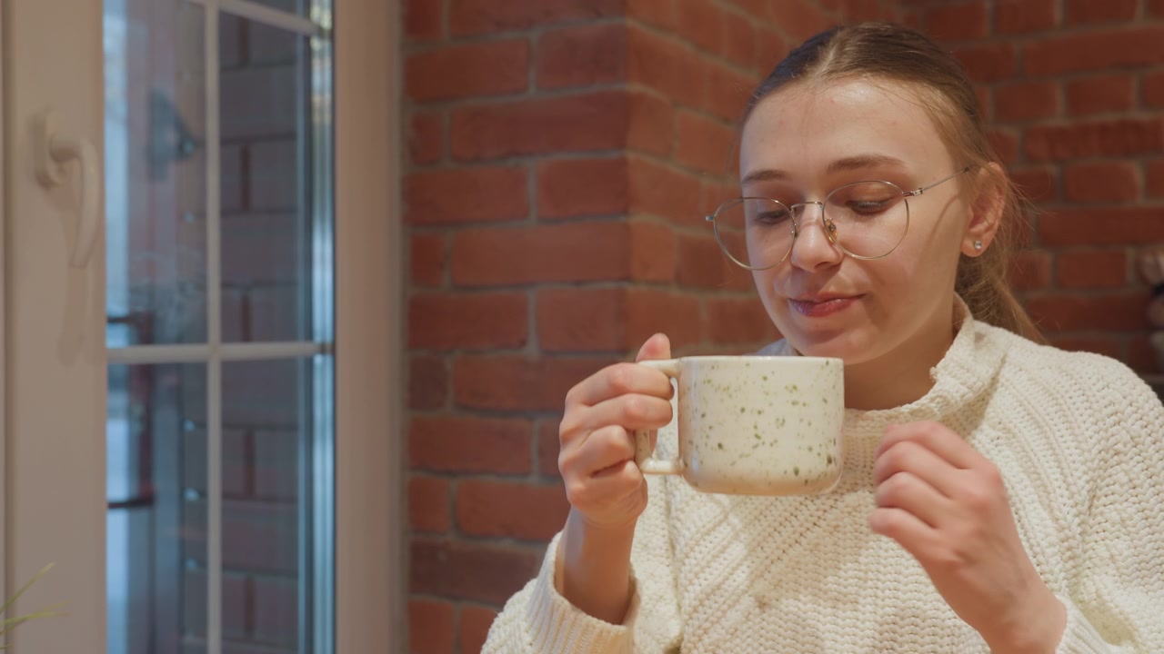 Young Woman Clinks Mugs and Sips Hot Drink