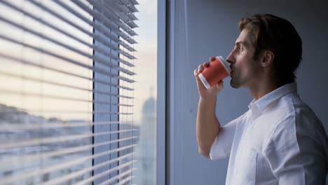 Seitenansicht-Eines-Jungen-Kaukasischen-Männlichen-Managers,-Der-Kaffee-Am-Fenster-In-Einem-Modernen-Büro-4K-Trinkt