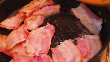 frying bacon in a pan with wooden spoon