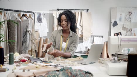 woman designer sitting at the table with laptop computer in her studio and choosing the cloth for a new collection