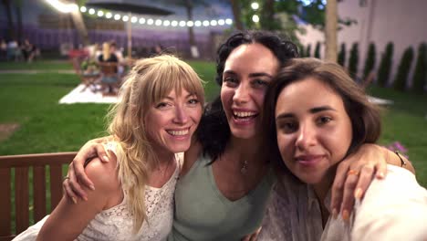 Three-Attractive-Women-Met-In-Veranda-Cafe-Outdoors-Taking-Selfie-Photo-Or-Video-On-Smartphone