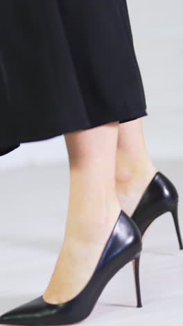 elegant classic black shoes demonstration. woman in long black skirt showing the high-heeled stiletto footwear. white backdrop. vertical video