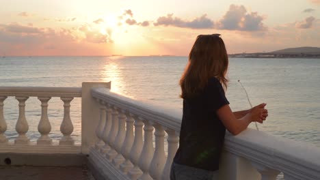 mujer viendo la puesta de sol sobre el mar desde un balcón