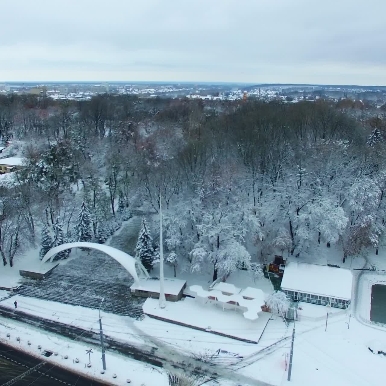 Central entrance with the arch to the city park. Trees in snow and city panorama from aerial view