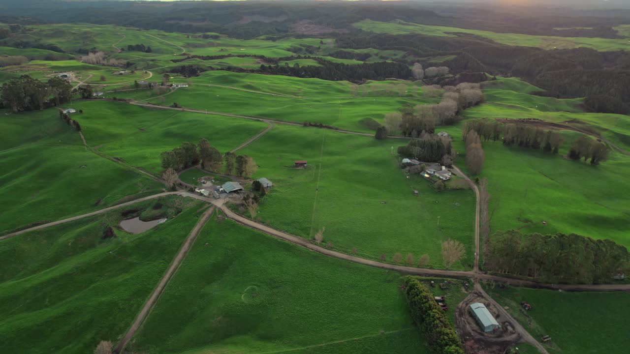 Aerial view of a sprawling farm landscape in New Zealand with lush green fields, rural roads, and farm buildings. A serene snapshot of countryside life and agricultural beauty