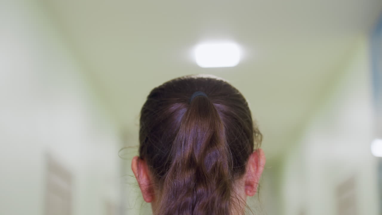 Therapist with long ponytail walks down well-lit hallway toward entrance door with faint Russian text posted shuts door gently after entering bright clinical environment with soft overhead lights