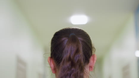 therapist with long ponytail walks down well-lit hallway toward entrance door with faint russian text posted shuts door gently after entering bright clinical environment with soft overhead lights