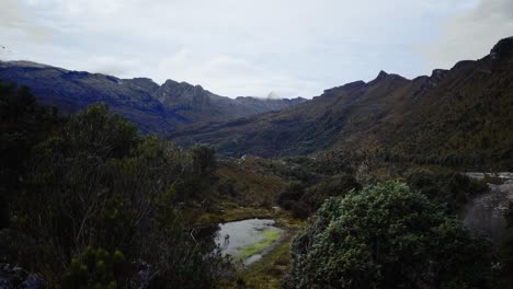 The-camera-captures-a-scenic-view-of-a-serene-pond,-nestled-amid-lush-greenery-with-a-breathtaking-vista-of-expanding-rocky-mountains-seen-from-a-unique-angle