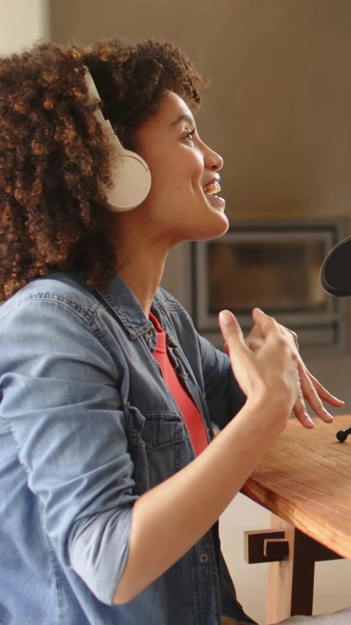 Vertical video: Smiling woman in denim jacket and white headset, facing mic and podcasting at home