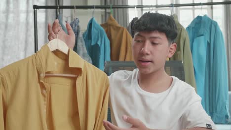 close up of asian man online seller recommending a shirt while using computer for selling clothes at home