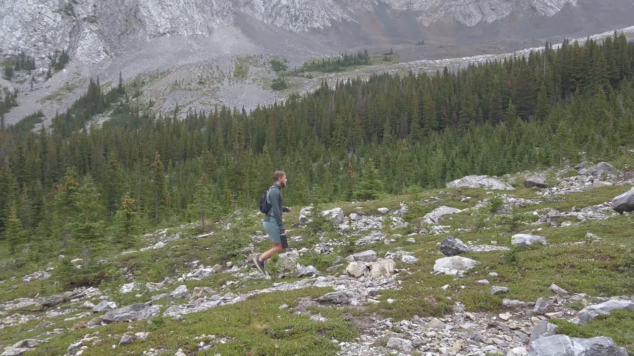 En turgåer som går opp et fjell ved en skog i Rocky Mountains, Kananaskis, Alberta, Canada.
