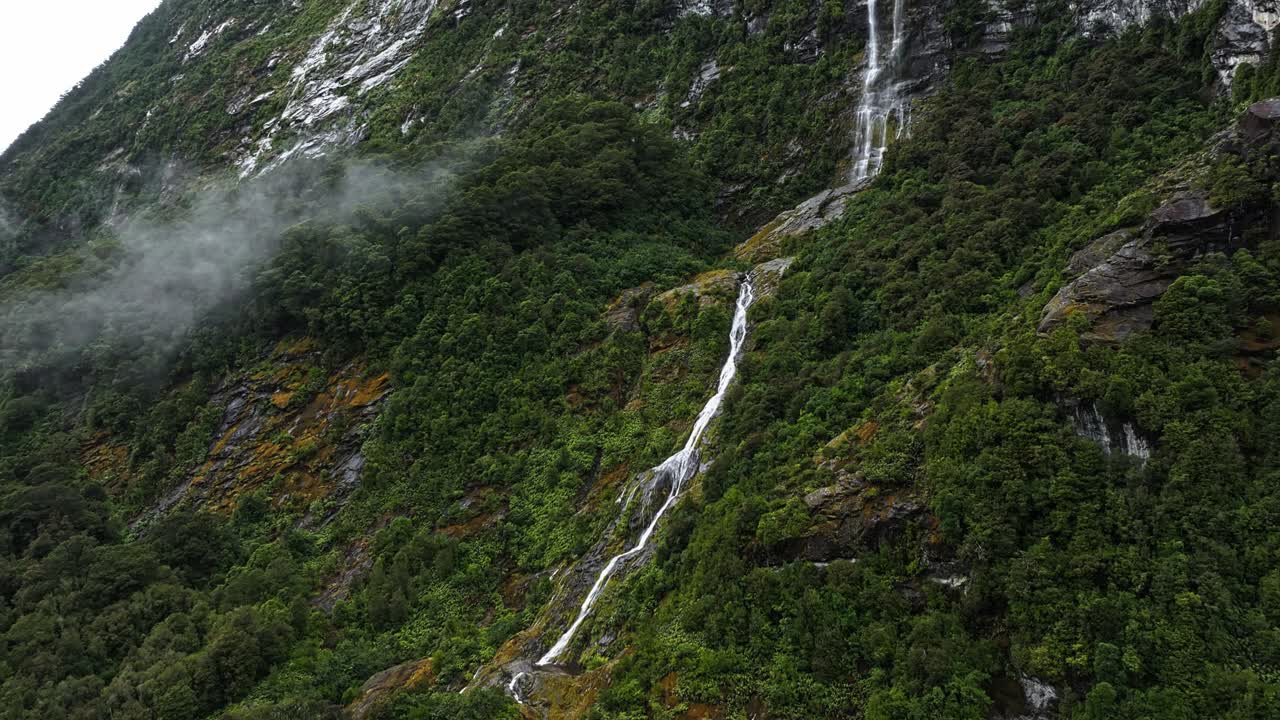Ripresa aerea con parallasse di un sottile rivolo di cascata che scende lungo le montagne scenografiche in Nuova Zelanda.