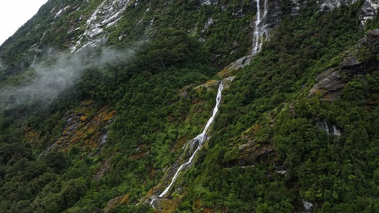 Ripresa aerea con parallasse di un sottile rivolo di cascata che scende lungo le montagne scenografiche in Nuova Zelanda.