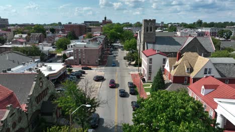 Aerial-footage-of-cars-traveling-down-a-residential-suburb-street-under-sunny-blue-sky