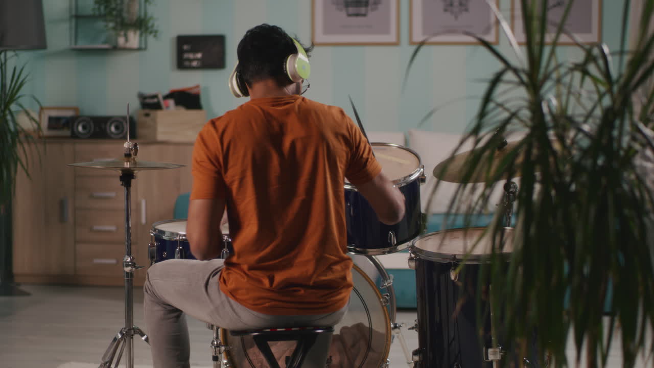 Anonymous Guy Playing Drums at Home back View of Unrecognizable Male Drummer in Casual Clothes and Wireless Headphones Playing Rhythm on Drums in Living Room at Home