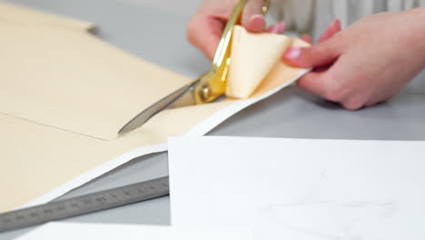 young female designer with tape-line on her neck standing in dressmaking studio and drawing lines with chalk and rule. female couturier in atelier cutting out a pattern for future clothes.