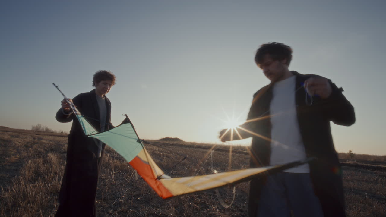 Couple Preparing Colorful Kite Together in Open Field at Sunset