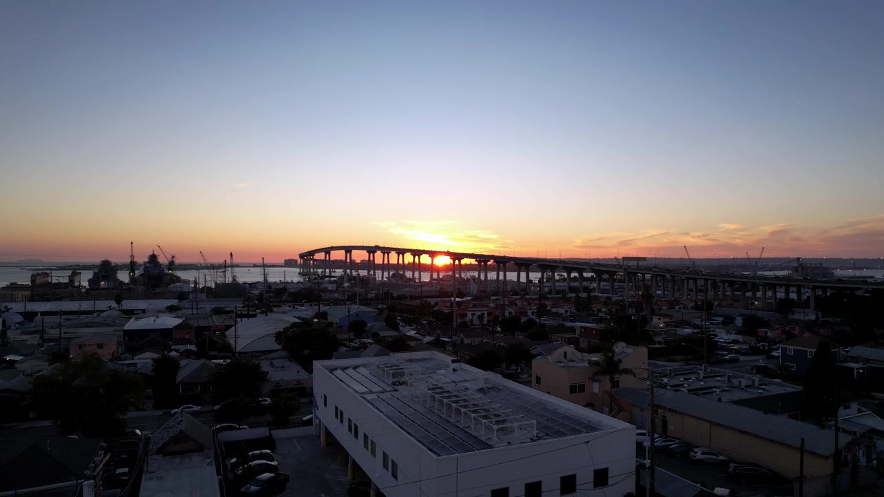 Drone pulling back from cars driving on the Coronado Bridge at sunset in San Diego California with warm evening light.