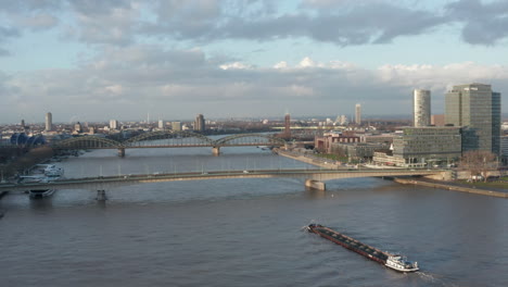 Aerial-footage-of-Rhine-river-and-its-bridges.-Large-cargo-ship-driving-under-busy-road-bridge.-Cologne,-Germany