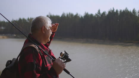 fisher-is-choosing-place-for-angling-on-river-standing-on-high-coast-holding-spin-fishing-rod-medium-portrait