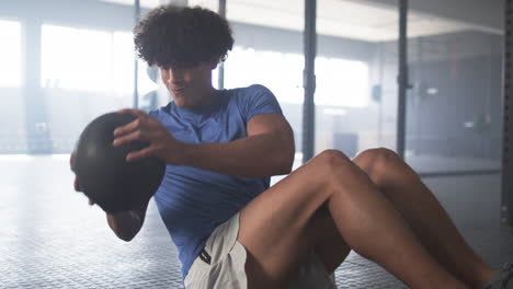 exercising in gym, man doing sit-ups with medicine ball, focusing on fitness