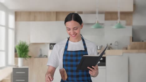 happy indian housewife making food from recipe book